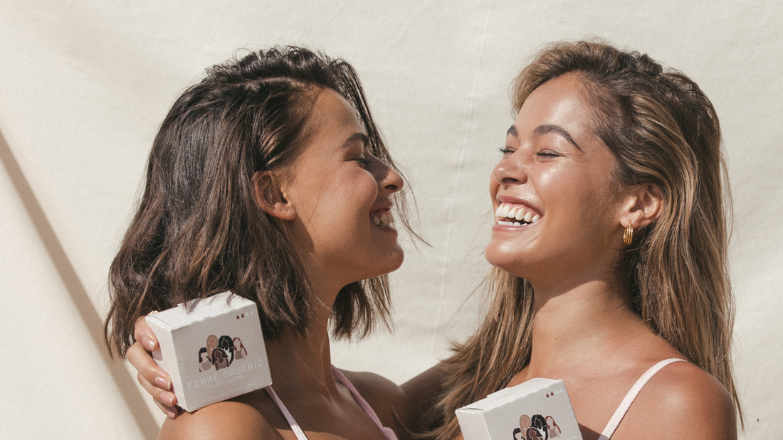 Two young women smiling and holding Femme Organic period care boxes, celebrating confidence and support during the first period journey. Empowering menstruators with sustainable and organic period products.
